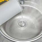 a person pouring hot water down the kitchen sink drain