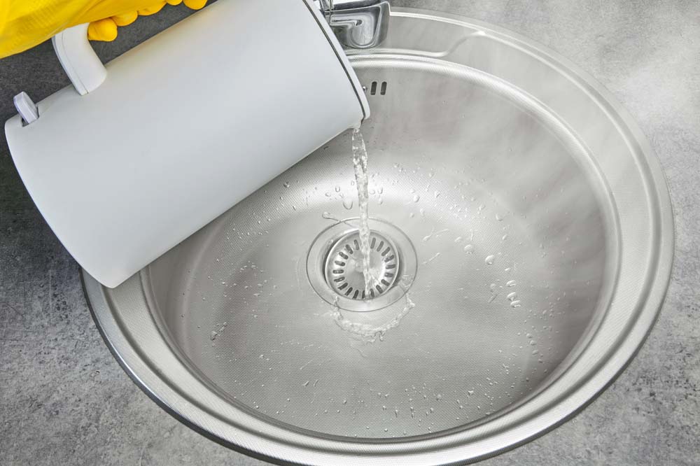 a person pouring hot water down the kitchen sink drain