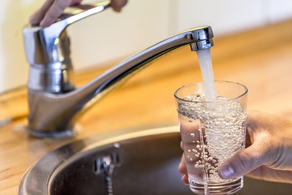person filling a drinking glass with tap water